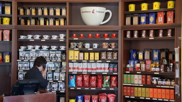 Ein Regal voller Julius Meinl Kaffee, Tee und Tassen in einem Geschäft.