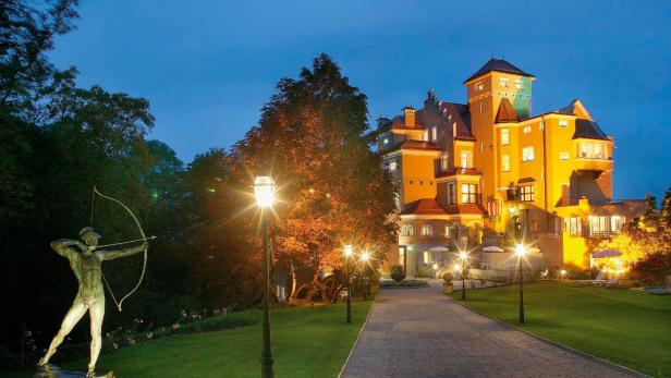 Eine Statue eines Bogenschützen steht vor einem beleuchteten Schloss in der Abenddämmerung.