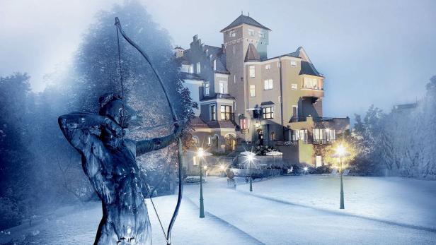 Eine Statue eines Bogenschützen vor einem beleuchteten Schloss im Winter.