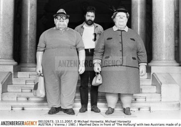 Manfred Deix vor der Hofburg mit zwei österreichischen Figuren.