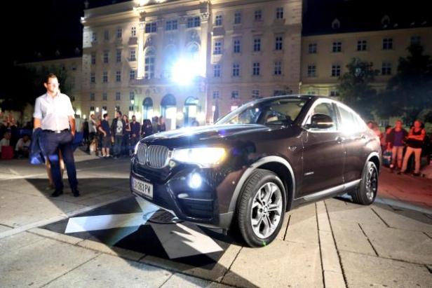 Ein brauner BMW steht auf einem Platz mit Menschen im Hintergrund.