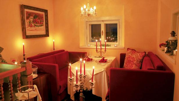 Ein gemütlicher Essbereich mit roter Sitzecke und Kerzenlicht.