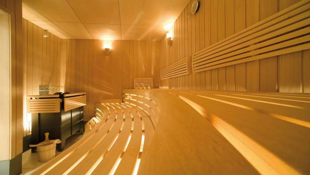 Innenansicht einer Sauna mit Holzbänken und einem Saunaofen.