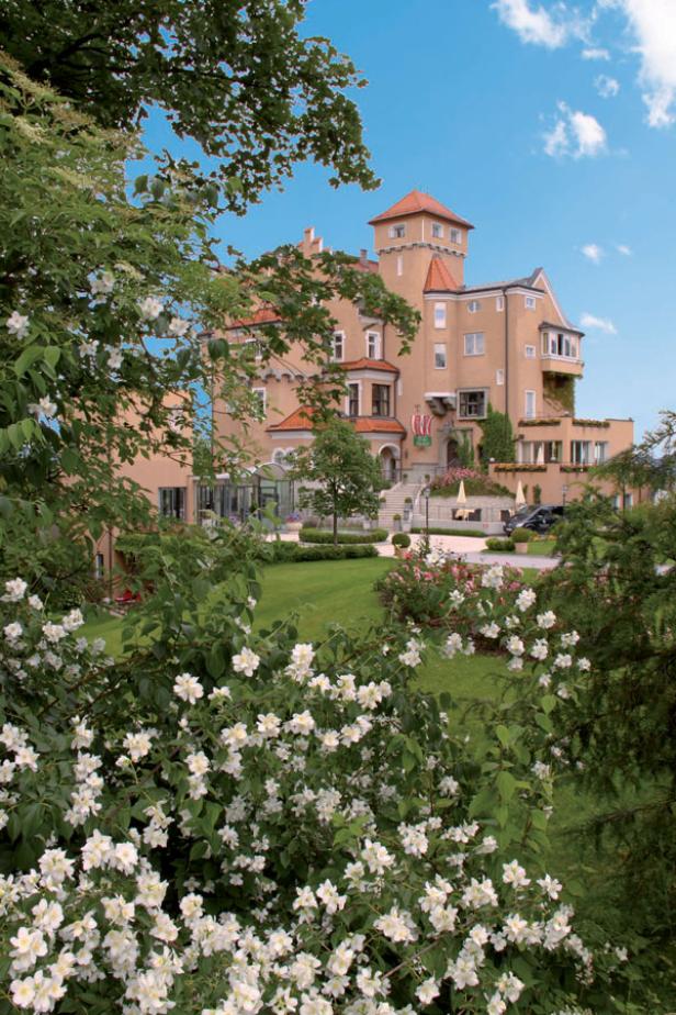 Ein Schloss mit einem Turm und einem gepflegten Garten im Vordergrund.