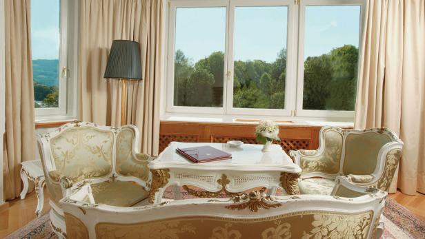 Ein elegantes Wohnzimmer mit antiken Möbeln und Blick auf eine grüne Landschaft.