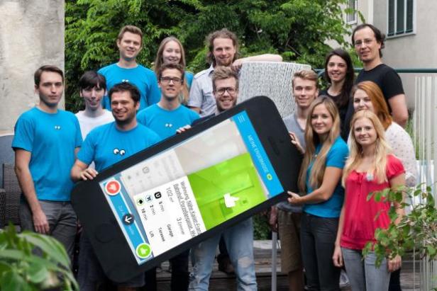 Eine Gruppe von Personen hält ein übergroßes Smartphone mit einer Immobilien-App in die Höhe.