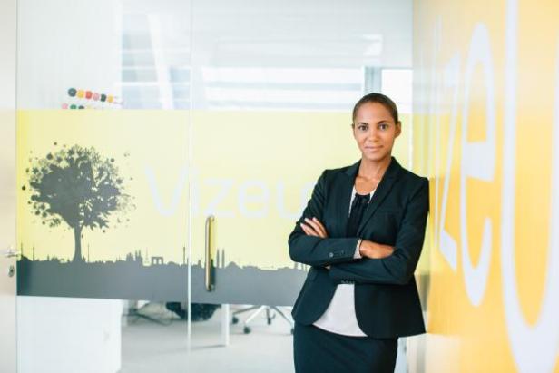 Eine Frau im Hosenanzug steht vor einer Wand mit dem Schriftzug „Vizeu“.