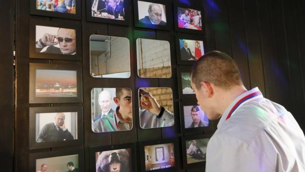 Ein junger Mann betrachtet eine Wand mit Fotos und Spiegeln, darunter Bilder von Putin.