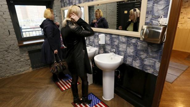 Zwei Frauen in einem Badezimmer mit Waschbecken und Spiegeln, dekoriert mit Jeans-Motiven.