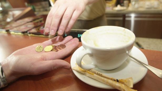 Eine Hand hält Münzen neben einer fast leeren Tasse Cappuccino.