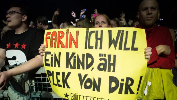 Zwei Konzertbesucher halten ein gelbes Schild mit der Aufschrift „Farin, ich will ein Kind, äh Plek von Dir!“.