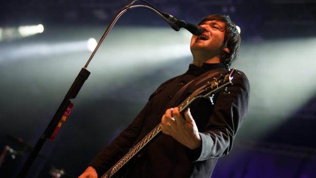 Ein Mann singt mit Gitarre auf einer Bühne in ein Mikrofon.