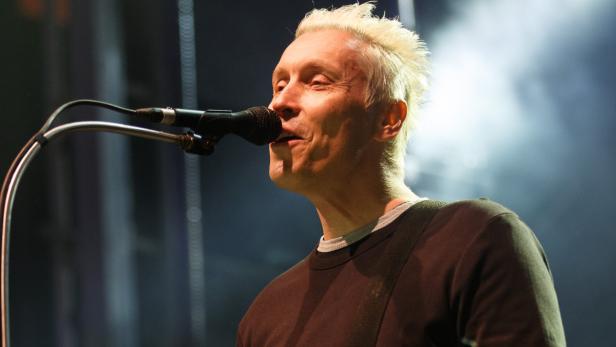 Ein Mann mit blonden Haaren singt in ein Mikrofon.
