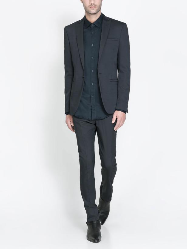 Ein Mann in einem dunklen Anzug und Hemd geht auf einem weißen Hintergrund.