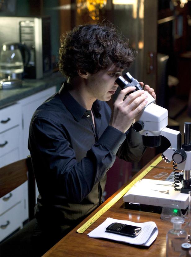 Ein Mann mit dunklem Haar blickt durch ein Mikroskop.