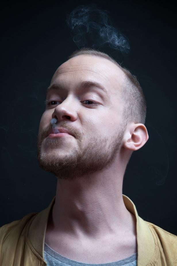 Ein Mann mit Bart pustet Rauch in die Luft.