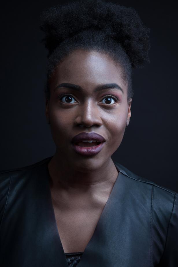 Eine Frau mit dunkler Haut und offenem Mund blickt überrascht in die Kamera.