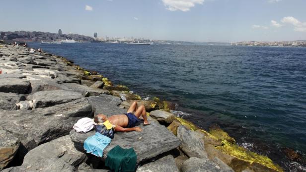 Ein Mann liegt auf Felsen am Ufer und sonnt sich.