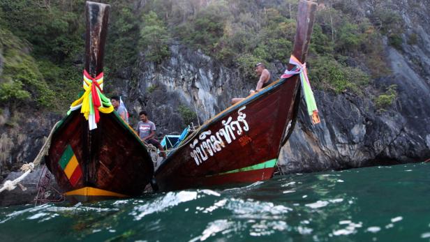 Zwei traditionelle thailändische Longtail-Boote liegen vor einer felsigen Küste im Wasser.