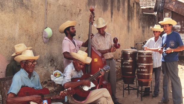 Eine kubanische Musikgruppe spielt im Freien mit Gitarren, Bass, Maracas und Trommeln.