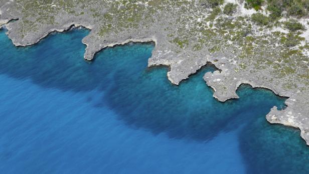 Die zerklüftete Küste einer tropischen Insel trifft auf das türkisfarbene Meer.