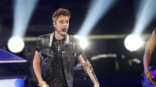 Justin Bieber tritt in einer silbernen Weste und goldenen Accessoires auf einer Bühne auf.