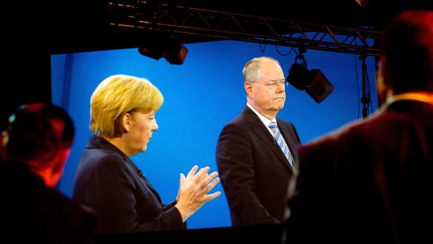 Angela Merkel und ein Mann im Anzug stehen vor einer blauen Leinwand.
