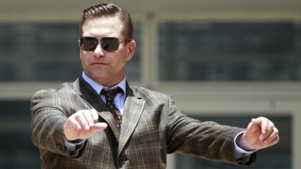 Ein Mann mit Sonnenbrille und Anzug gestikuliert mit den Händen.