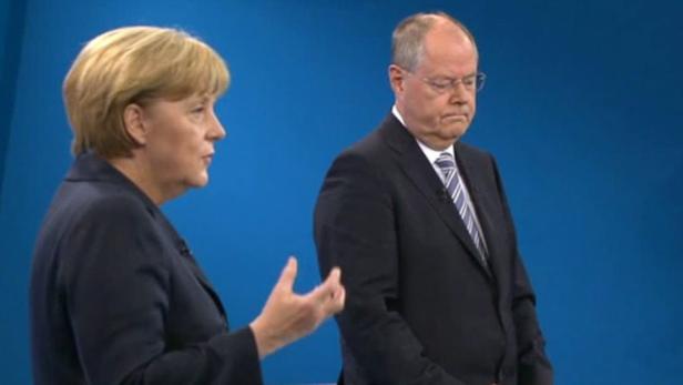 Angela Merkel spricht, während ein Mann im Anzug neben ihr steht.