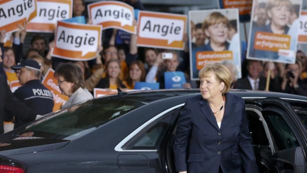 Angela Merkel steigt aus einem Auto, während Unterstützer Schilder mit ihrem Namen hochhalten.