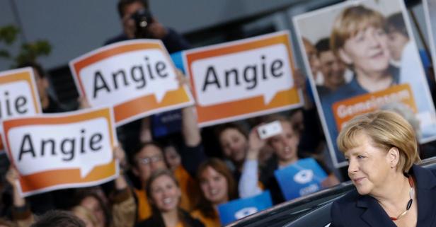 Angela Merkel bei einer Veranstaltung, umgeben von Anhängern mit „Angie“-Schildern.