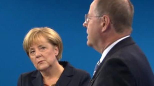 Angela Merkel während einer Veranstaltung mit einem Mann im Anzug.