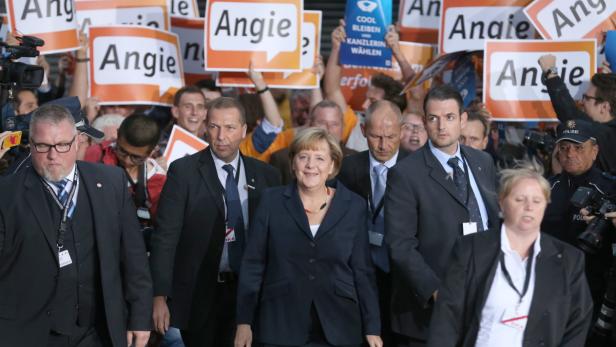 Angela Merkel inmitten von Sicherheitsleuten und Anhängern mit „Angie“-Schildern.