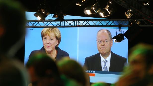 Angela Merkel und Peer Steinbrück auf einem Bildschirm während einer Veranstaltung.