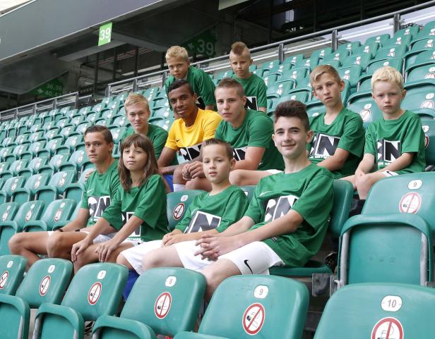 Eine Gruppe von Kindern sitzt auf den grünen Sitzen eines Stadions.