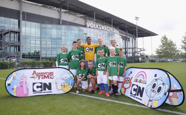 Eine Gruppe junger Fußballspieler posiert vor der Volkswagen Arena mit „Adventure Time“- und „Gumball“-Bannern.