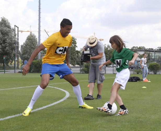 Ein junger Mann und ein Kind spielen Fußball, während ein Kameramann sie filmt.