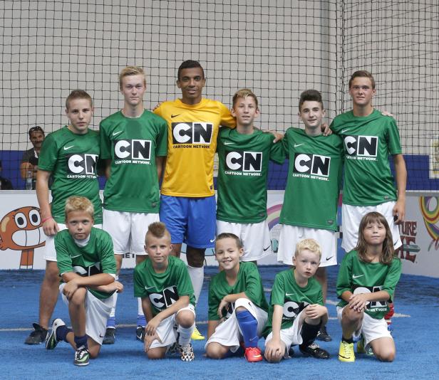 Eine Gruppe von Kindern und ein junger Mann posieren in grünen und gelben Cartoon Network-Trikots für ein Foto.