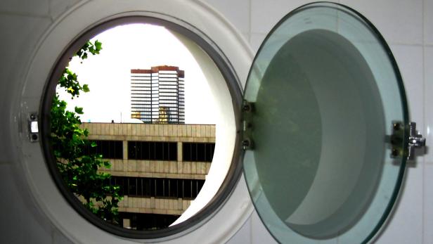 Blick aus einem Bullauge auf ein Gebäude und einen Wolkenkratzer.