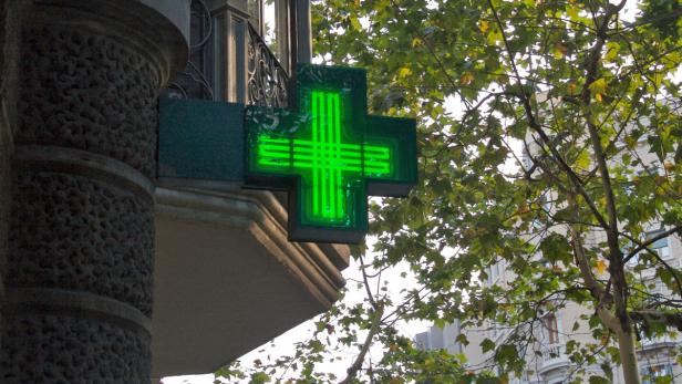 Ein grünes Apothekenkreuz leuchtet an der Ecke eines Gebäudes.