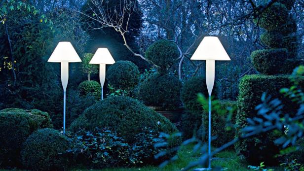 Drei beleuchtete Stehlampen stehen in einem üppigen, grünen Garten.