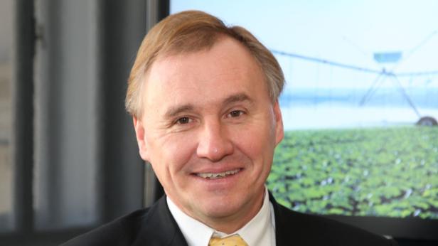 Ein Mann im Anzug lächelt vor einem Bildschirm mit einem Feld und einer Bewässerungsanlage.