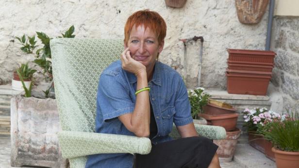 Eine Frau mit roten Haaren sitzt in einem Sessel im Freien.