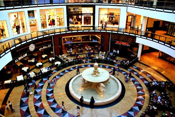 Blick von oben auf eine belebte Einkaufspassage mit einem Springbrunnen in der Mitte.