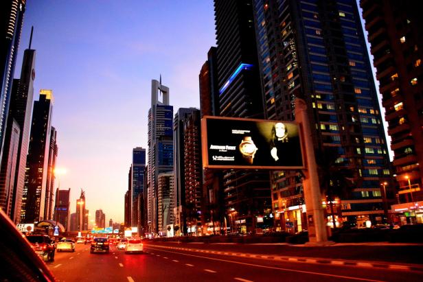 Eine belebte Straße in Dubai mit Wolkenkratzern und einem Werbeplakat.