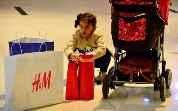 Ein Mädchen hockt neben Einkaufstüten und einem Kinderwagen.