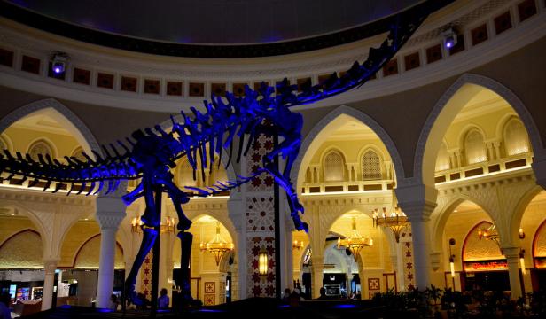 Ein blau beleuchtetes Dinosaurierskelett hängt in einem Einkaufszentrum mit arabischer Architektur.