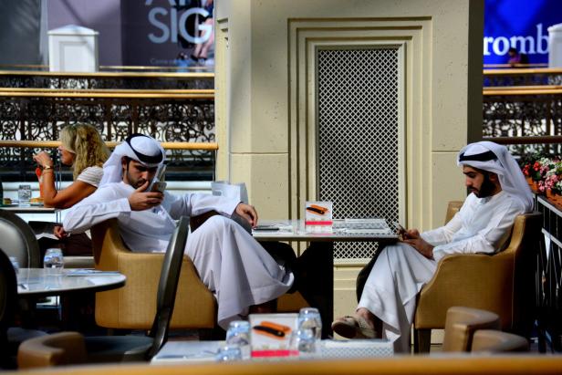 Zwei Männer in traditioneller arabischer Kleidung sitzen in einem Café und nutzen ihre Smartphones.