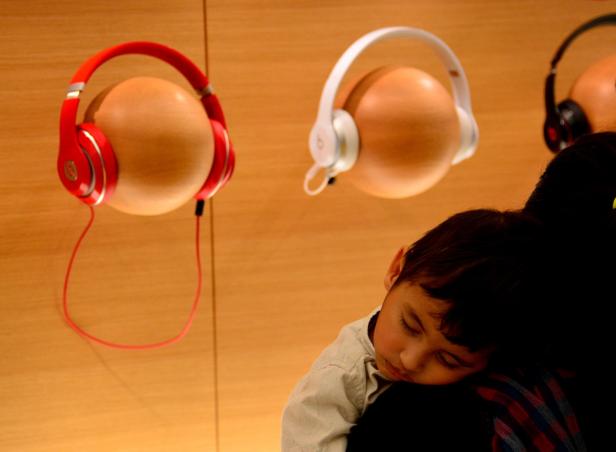 Ein schlafender Junge lehnt an der Schulter einer Person vor einer Wand mit Kopfhörern.