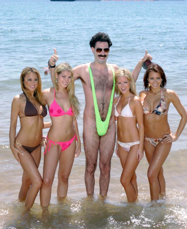 Sacha Baron Cohen als Borat posiert mit vier Frauen am Strand.